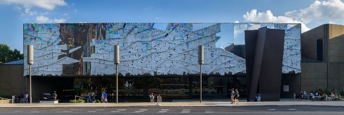 the facade of a large building, covered in textured materials and mirrors that reflect the sky.